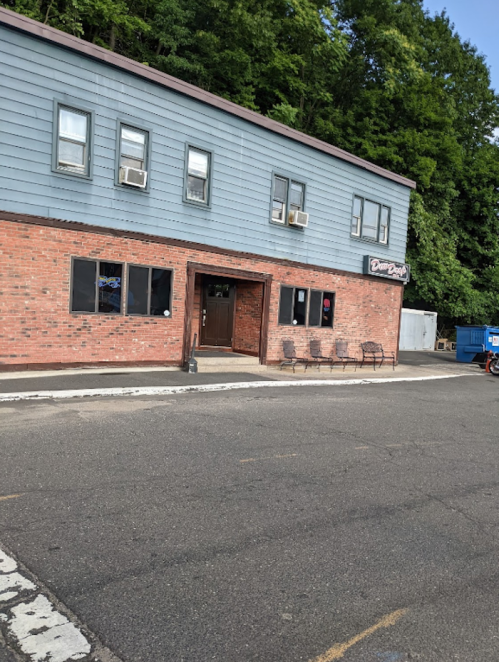 A brick building with gray siding, featuring windows and a door, along with outdoor seating and a dumpster nearby.