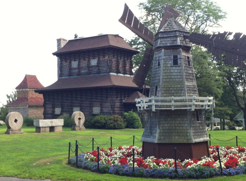 A historic building with a windmill and flower beds in a green park setting.