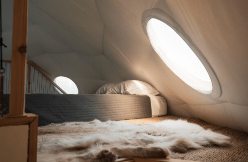 Cozy interior of a tent-like room with circular windows, a bed, and a soft rug on the floor.