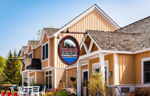 A charming bakery and deli with a wooden exterior and a sign featuring a bear, surrounded by greenery.