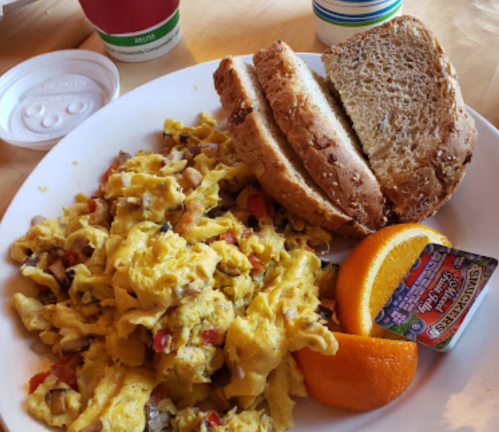 A plate with scrambled eggs mixed with vegetables, two slices of bread, and orange slices, accompanied by a small butter packet.