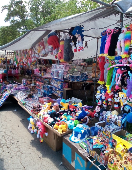 A vibrant market stall filled with colorful plush toys, games, and various merchandise under a canopy.