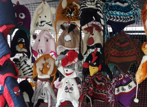 A variety of colorful knitted hats displayed on a rack, featuring animal designs and playful patterns.