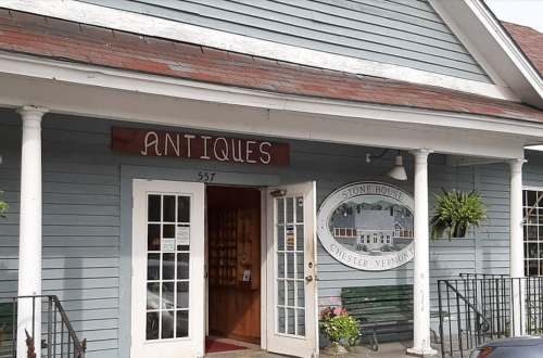 A quaint antique shop with a sign reading "Antiques" and a welcoming entrance in Chester, Vermont.