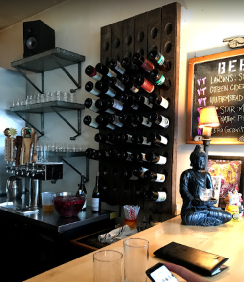 A bar with a wine rack, beer taps, glasses, and a Buddha statue, creating a cozy atmosphere.