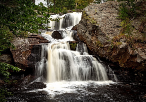 A serene waterfall cascading over rocky terrain, surrounded by lush greenery and a tranquil pool below.