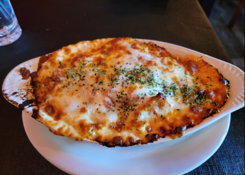 A baked dish with melted cheese, herbs, and a golden crust, served in a white oval dish on a black table.