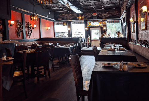 A cozy restaurant interior with wooden tables, chairs, and red walls, featuring a view of the entrance and staff.