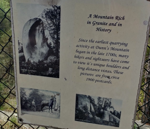Sign about Dunn's Mountain history, featuring images of early quarrying and hikers, with a granite boulder backdrop.
