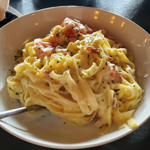 A bowl of creamy fettuccine pasta topped with diced tomatoes and herbs, served with a fork on the side.