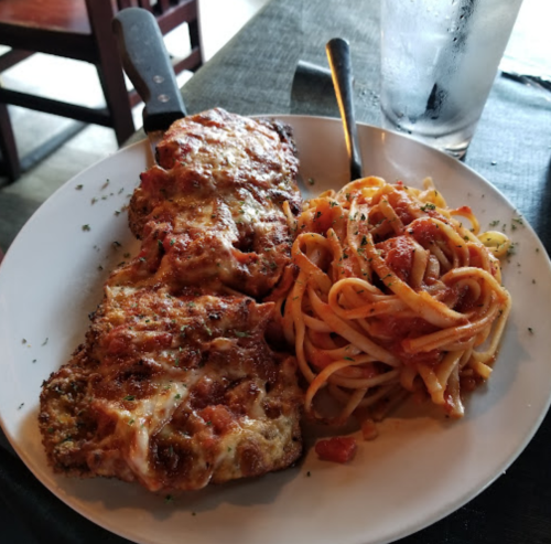 A plate of cheesy baked chicken with marinara sauce, served alongside a portion of spaghetti in tomato sauce.