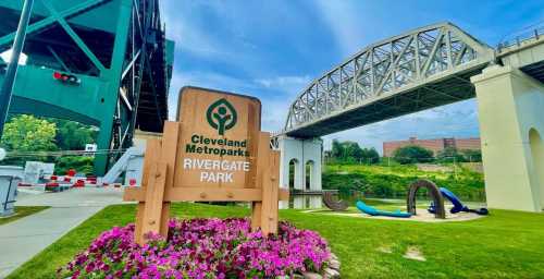 Sign for Rivergate Park in Cleveland Metroparks, with a bridge overhead and colorful flowers in the foreground.