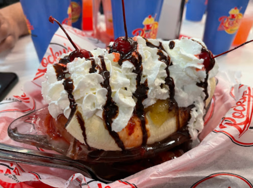 A banana split topped with whipped cream, chocolate syrup, and cherries, served in a glass dish.