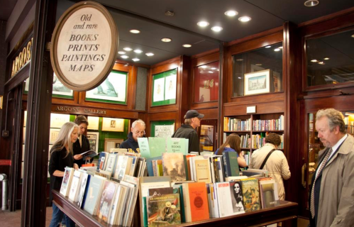 A cozy bookstore with shelves of books, people browsing, and a sign for old and rare books, prints, and maps.
