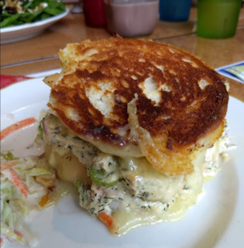 A toasted sandwich with melted cheese and a creamy filling, served with a side of coleslaw on a white plate.