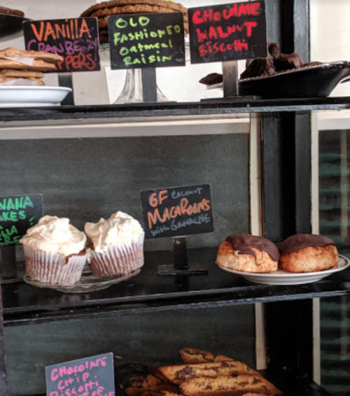 A display of assorted baked goods, including cupcakes, cookies, and macarons, with colorful labels.