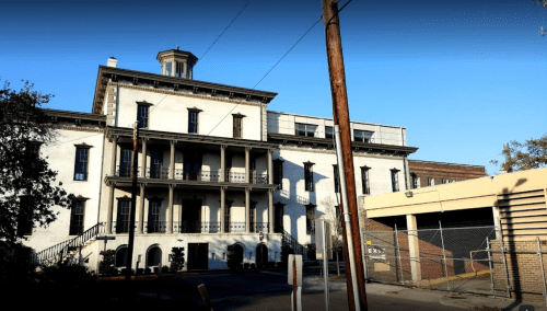 Historic white building with multiple balconies, a tower, and a clear blue sky in the background.