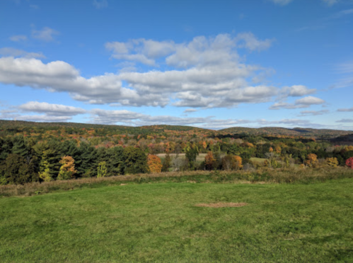A scenic view of rolling hills covered in autumn foliage under a blue sky with fluffy clouds.