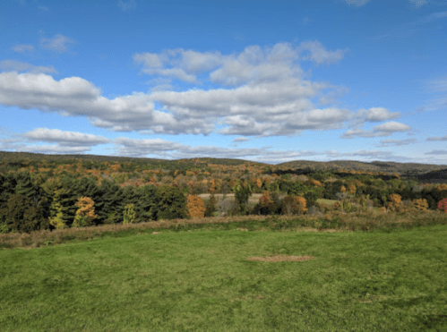 A scenic view of rolling hills covered in autumn foliage under a blue sky with fluffy clouds.