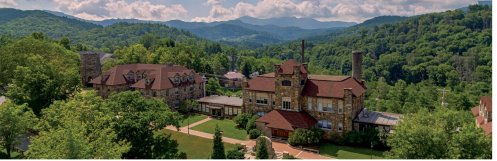 A scenic view of a stone building surrounded by lush greenery and mountains under a partly cloudy sky.
