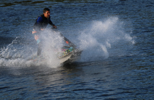 A person riding a jet ski on a lake, creating splashes of water against a blue background.