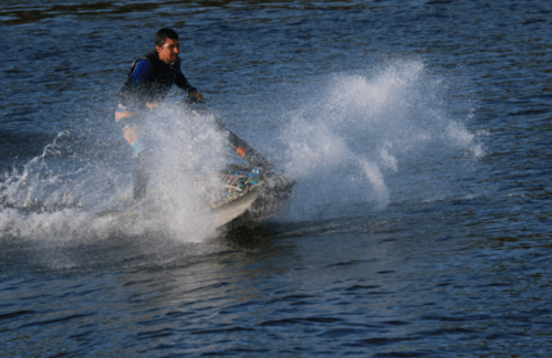 A person riding a jet ski on a lake, creating splashes of water against a blue background.