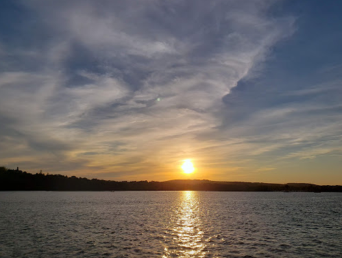 A serene sunset over a calm lake, with colorful clouds reflecting on the water's surface.