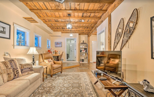 Cozy living room with wooden beams, a sofa, armchair, TV, and decorative snowshoes on the wall. Warm, inviting atmosphere.