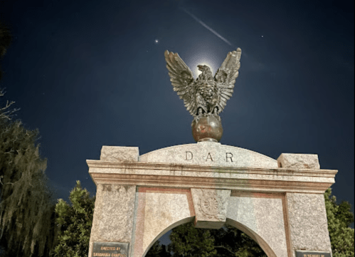 A monument featuring an eagle atop an arch, illuminated by moonlight against a night sky.