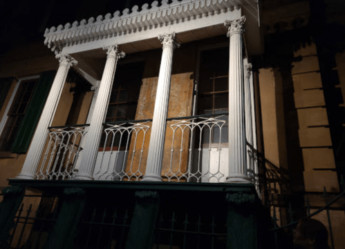 A historic building with white columns and a balcony, illuminated at night against a dark background.