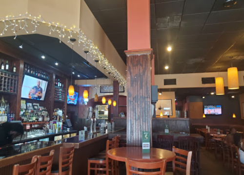 Interior of a restaurant featuring a bar, wooden tables, and warm lighting with decorative string lights.