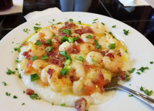 A plate of shrimp and grits topped with green onions and bacon bits, garnished with parsley.