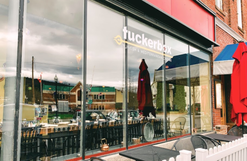Exterior view of Tuckerbox restaurant, featuring large windows, outdoor seating, and a red awning.