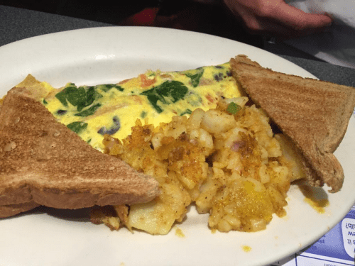 A plate with a spinach omelette, golden hash browns, and two slices of toasted bread.