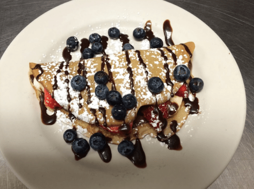 A delicious crepe filled with strawberries and blueberries, drizzled with chocolate sauce and sprinkled with powdered sugar.