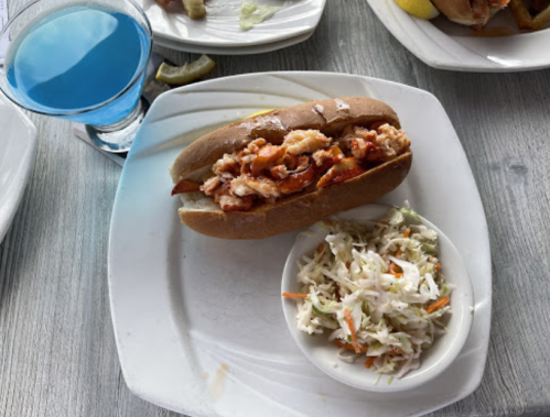 A sandwich filled with shredded meat on a plate, accompanied by a small bowl of coleslaw and a blue drink.