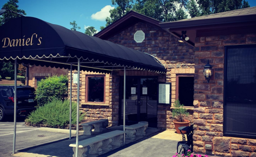 Exterior of Daniel's restaurant featuring a stone facade, awning, and outdoor seating area with plants.