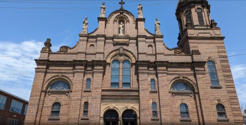 Historic brick church with ornate architecture, statues, and a tall bell tower against a blue sky.