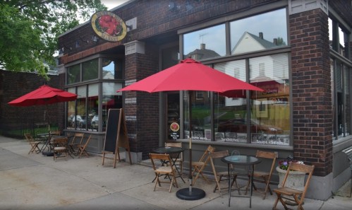 A cozy café with red umbrellas and outdoor seating, featuring large windows and a brick exterior.