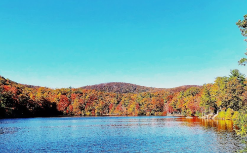 A serene lake surrounded by vibrant autumn foliage under a clear blue sky.