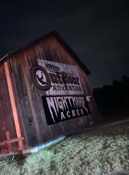 A wooden barn at night with signs for "Nomad's Outdoor Adventure" and "Nightmare Acres."