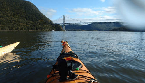 A kayak on calm water with a bridge in the background and hills covered in greenery under a clear blue sky.