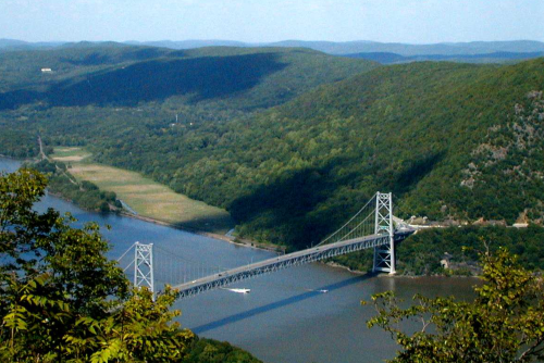 A scenic view of a suspension bridge spanning a river, surrounded by lush green hills and clear blue skies.