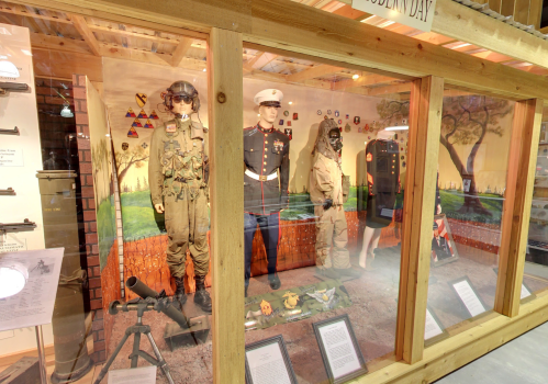 Display of military uniforms and equipment in a museum exhibit, showcasing various branches and historical artifacts.