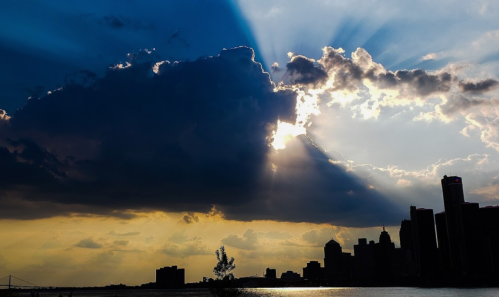 Dramatic clouds with sunlight streaming through, silhouetting a city skyline against a colorful sky.