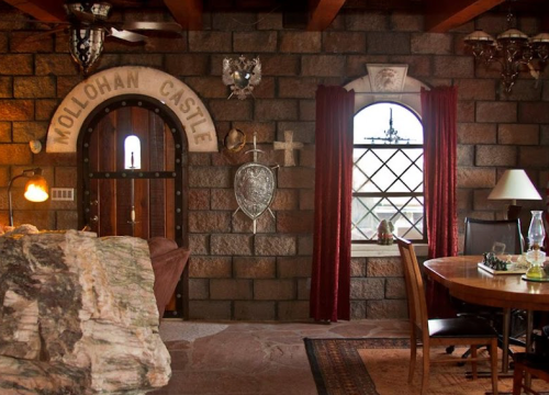 Interior of a rustic room featuring stone walls, a castle-themed door, a round window, and wooden furniture.