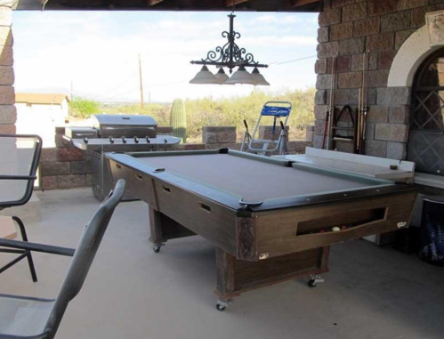 A covered outdoor space featuring a pool table, grill, and seating with a desert landscape in the background.