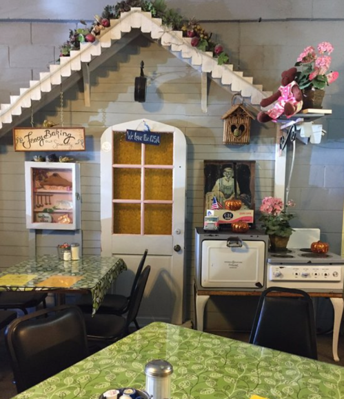 Cozy café interior featuring a decorative house facade, vintage decor, and green tablecloths.