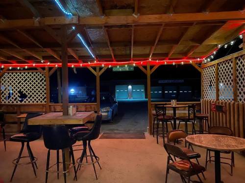 Cozy outdoor seating area with bar stools and tables, illuminated by string lights, overlooking a parking lot at night.
