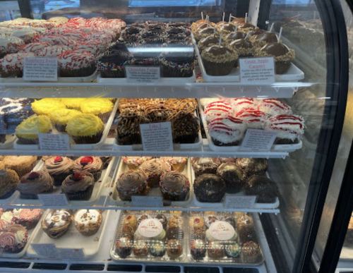 A display case filled with various colorful cupcakes and treats, including chocolate, vanilla, and red velvet options.